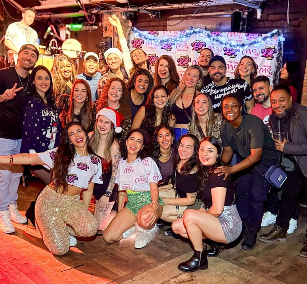 The Brazil FitDance crew posing together in front of the Gio and Mow banner at a Christmas party